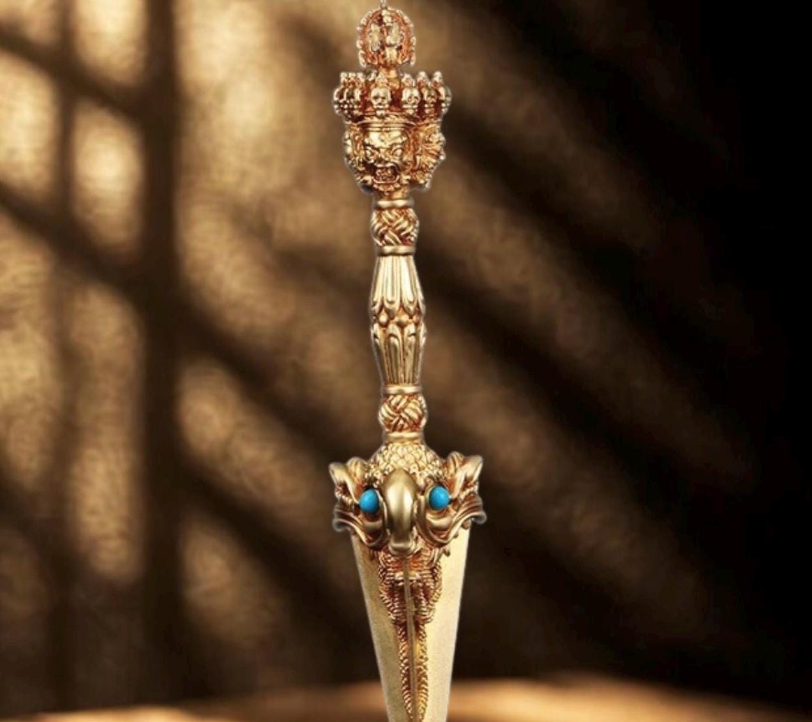 A gold colored metal ornament with a detailed design. The ornament features a central face with a crown and multiple smaller faces surrounding it. The ornament is intricately detailed and has a traditional design.